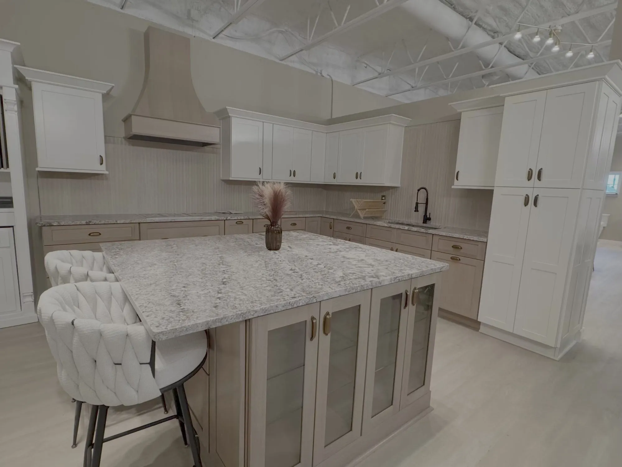 Kitchen display with a granite-look island, cream cabinetry, and range hood at Steel Valley Showroom